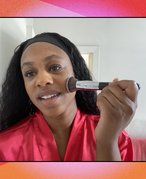 Picture of a person holding a stippling brush against their cheek, on a red graphic background