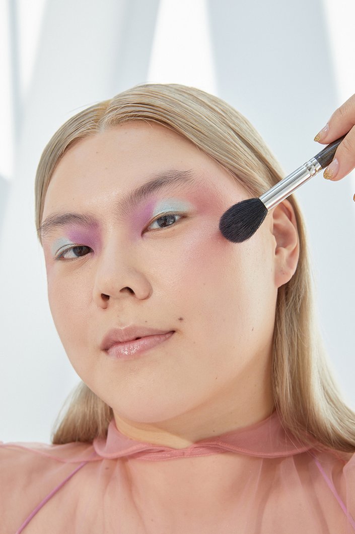 person applying blush to cheek with makeup brush