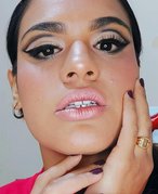 A person with dark hair pulled back looking at the camera, wearing a full face of makeup and cut crease eyeshadow