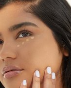 Person with long dark hair with foundation swatched under their eye in small dots
