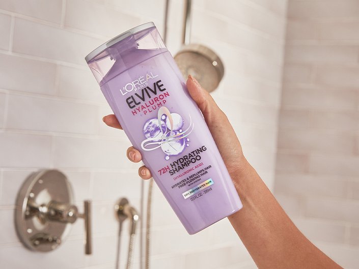 person holding loreal paris elvive shampoo with hyaluronic acid in the shower