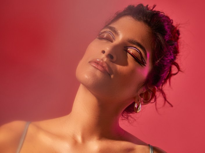 Image of a person with their head tilting up and brunette hair, looking up with eyes closed. The background is red.