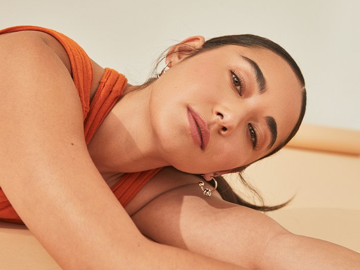 Picture of a model with dark hair in a ponytail, lying on their side