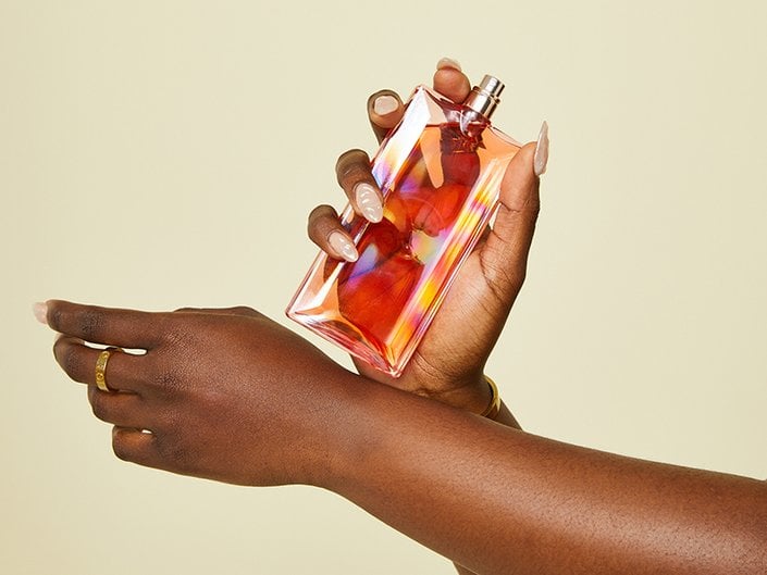 Picture of someone holding a bottle of perfume and rubbing their wrists together to apply